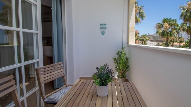A balcony with a wooden table, two potted plants, a bench, and a wall-mounted sign. - Imperial Puerto 3E - Terrace, Swimming Pool, 200m from the beach (Torremolinos)