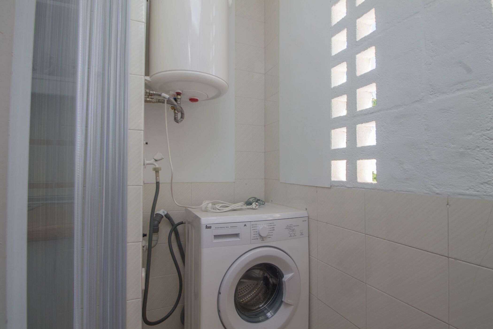 Une petite salle de bain équipée d’un lave-linge, d’un espace douche et d’une fenêtre à carreaux.
