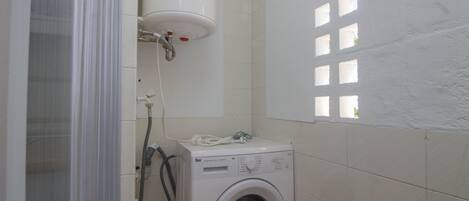Une petite salle de bain équipée d’un lave-linge, d’un espace douche et d’une fenêtre à carreaux.
