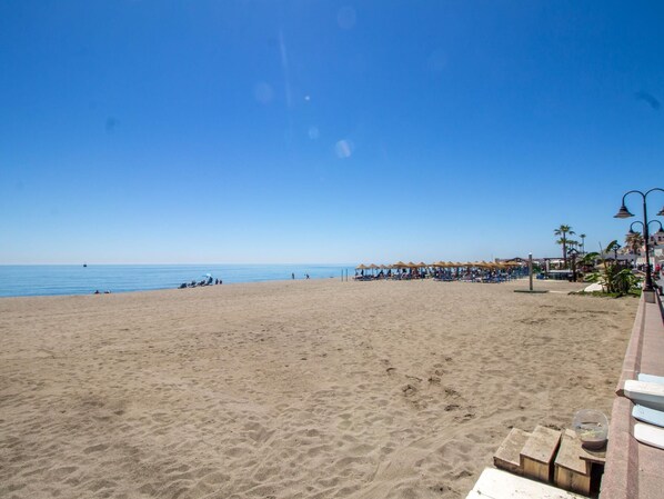 A beach with umbrellas and lounge chairs, a clear sky, and a calm sea.