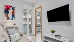 A modern living room with a sofa, a flat-screen TV, a white console table, and a colorful abstract painting. - Los Nidos - 1 bedroom, Terrace, 100 m from the beach (Torremolinos)