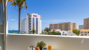 Un balcon avec une table dressée pour le petit-déjeuner, offrant une vue sur le paysage urbain et mettant en valeur un bâtiment emblématique de la chaîne RIU.