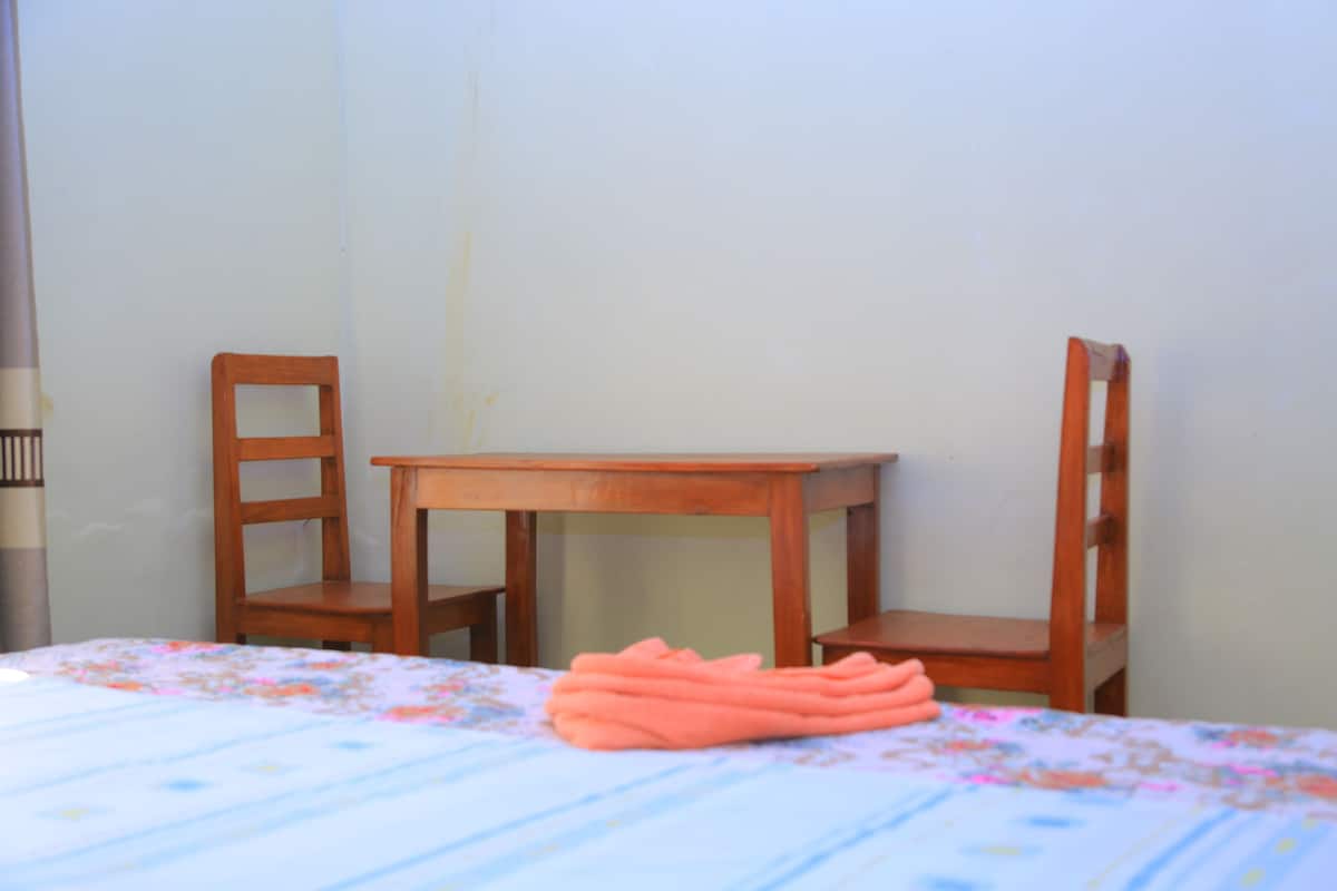 A room with a bed, two wooden chairs, and a small table.
