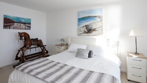 Quarto com cama, mesa de cabeceira, abajur, escultura de cavalo e duas pinturas na parede.