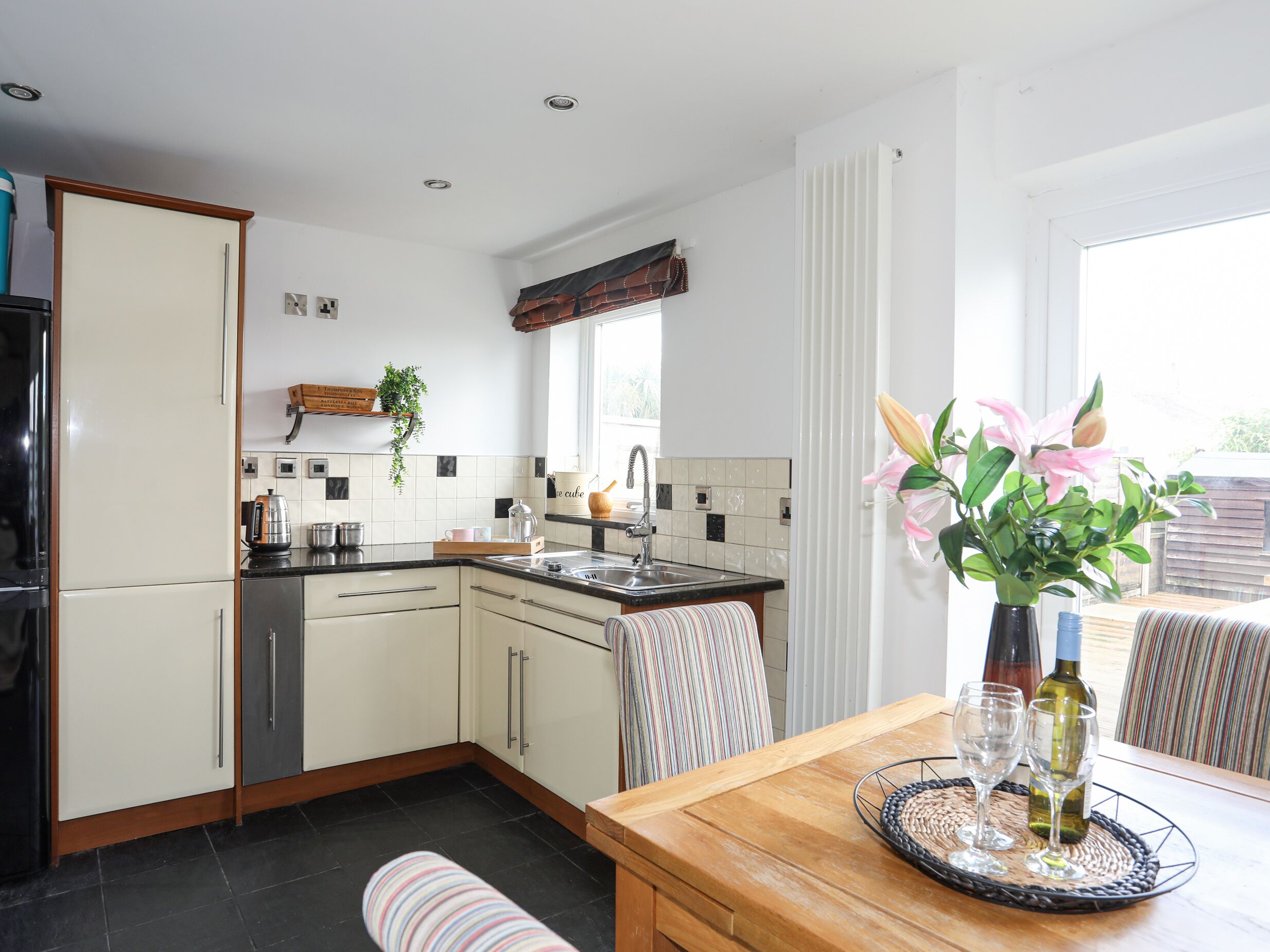 A modern kitchen with white cabinets, a black countertop, and a dining area with a wooden table and striped chairs.