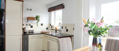 A modern kitchen with white cabinets, a black countertop, and a dining area with a wooden table and striped chairs.