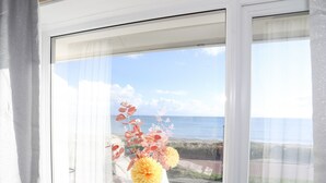 Uma janela com vista para o mar e um vaso branco com flores.