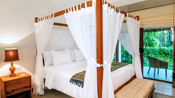Una cama con dosel con ropa blanca y un dosel, una mesita de noche de madera con una lámpara, y vista a zonas verdes a través de una puerta de cristal.