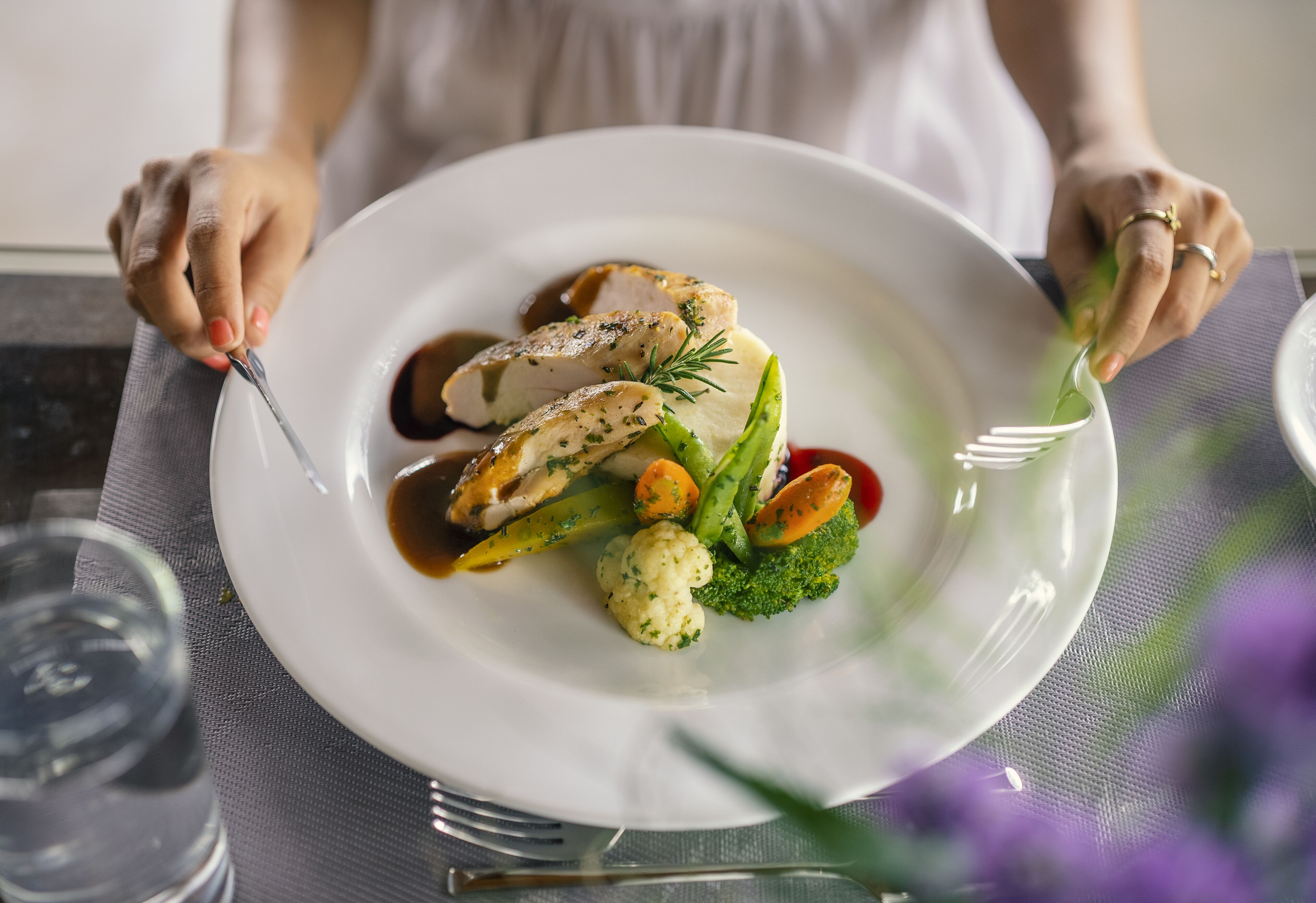 Una persona tiene un piatto bianco con un pasto composto da carne a fette, verdure e salsa.