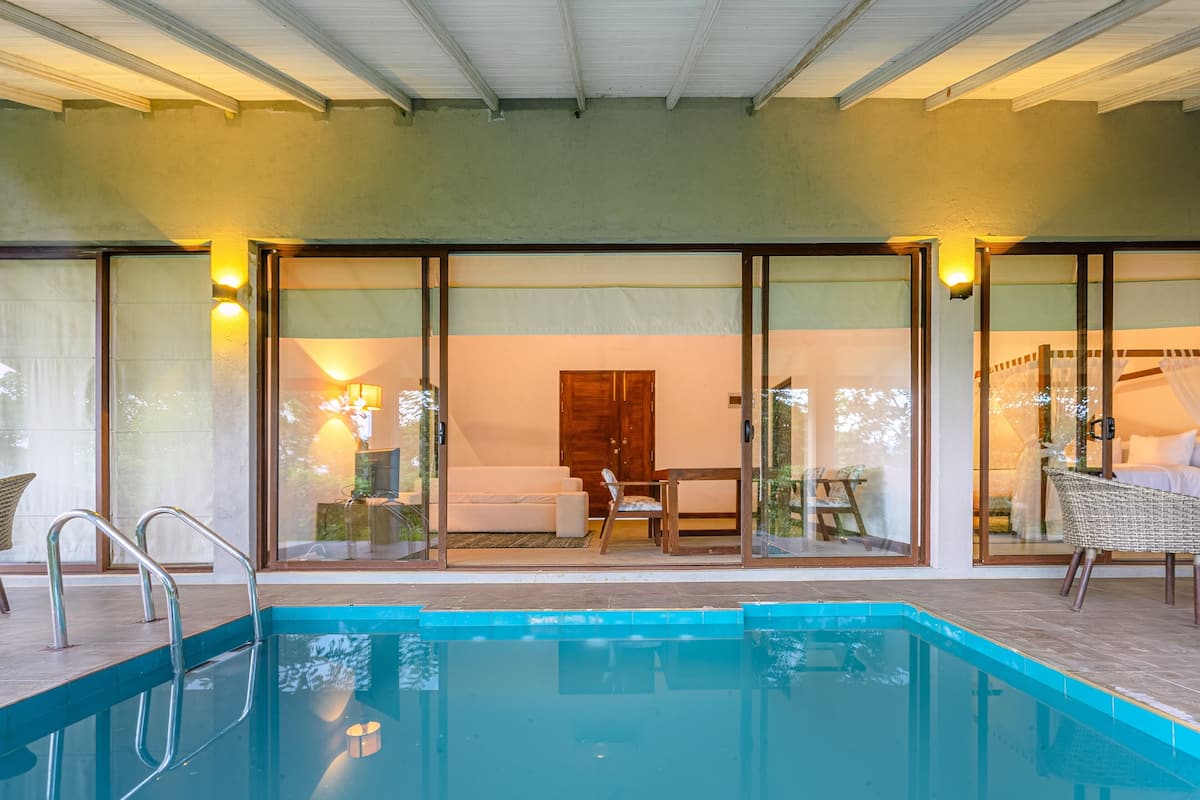 Piscina com portas de vidro que dão para um quarto com sofá, mesa de madeira e uma cadeira.