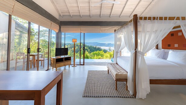 Un dormitorio con una cama grande, televisión, mesa de madera y vistas a zonas verdes y montañas.
