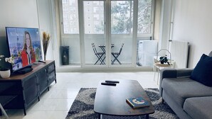 Una sala de estar moderna con televisor de pantalla plana, un sofá, una mesa de centro y vistas a un balcón con mobiliario exterior.