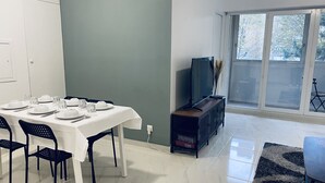 Un comedor con una mesa dispuesta para cuatro personas, un televisor sobre un mueble bajo y vistas al exterior a través de un ventanal amplio.