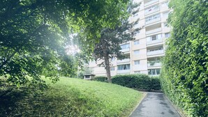 Un sendero conduce a un edificio residencial de varios pisos rodeado de abundante vegetación y árboles.