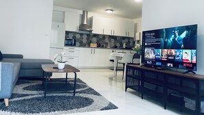 Una sala de estar moderna con un sofá gris, una mesa de centro y un televisor que muestra una selección de películas.