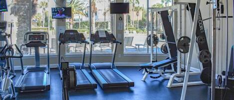 A gym with treadmills, weight machines, and a TV screen.