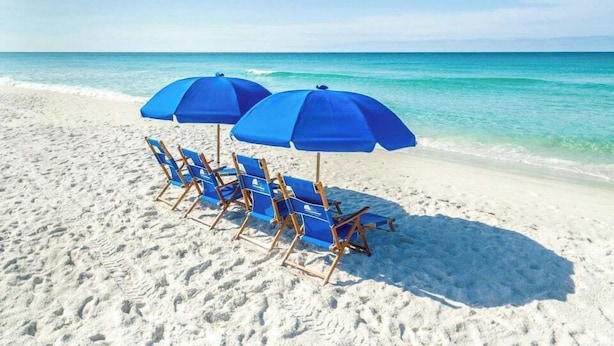 Una playa de arena blanca, una fila de sillas azules y dos sombrillas azules.