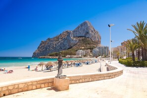 Une plage bordée d’une montagne rocheuse, avec des parasols et un sentier pavé de pierres.