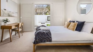 A bedroom with a bed, a desk, and a chair. There is a view of the outdoors through a door. - Elliston House (Kingscliff)