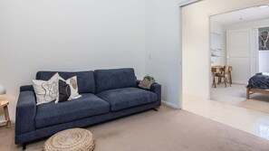 Un salon moderne avec un canapé bleu foncé, un petit pouf rond et une plante.