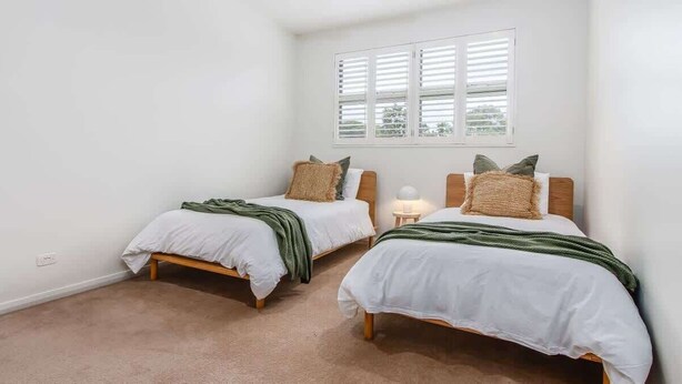 Un dormitorio con dos camas individuales, una ventana con persianas y una mesita de noche con lámpara.