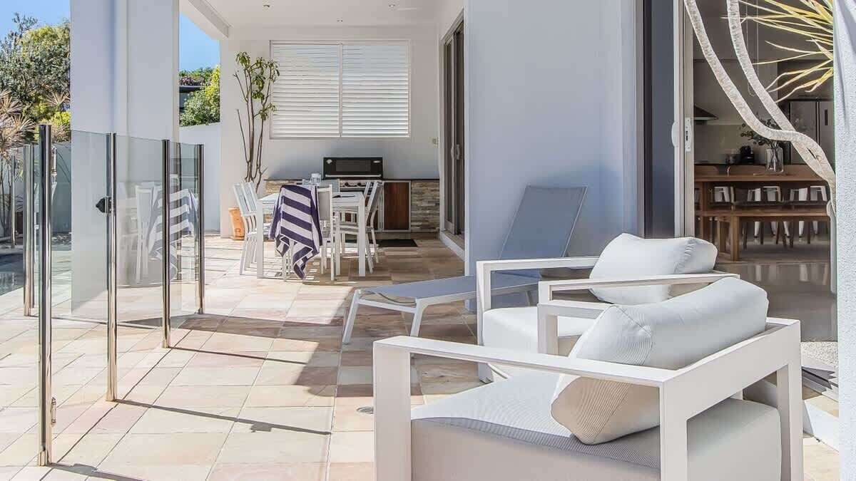 A modern outdoor seating area with white furniture, a dining table, and a kitchen in the background.