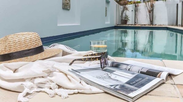 A poolside setting with a straw hat, a glass of water, and a magazine.