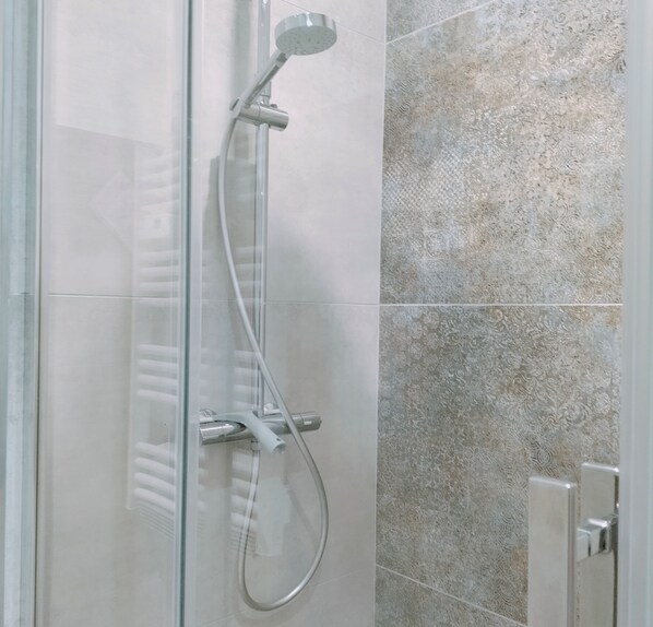 Ducha envuelta en vidrio con cabezal de ducha manual y llave montada en la pared.