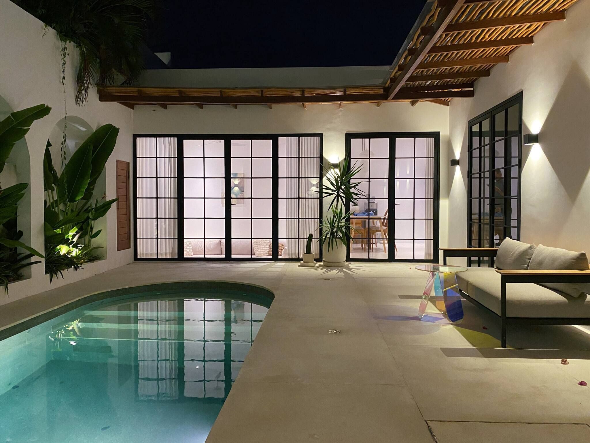 Una piscina con borde curvo, un sofá y un comedor con mesa y sillas.