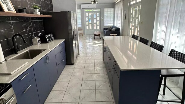 A modern kitchen with dark blue cabinets, a stainless steel refrigerator, and a large island with bar stools. - Experience Puerto Rico's Charm in style with modern comforts.  (Luyando)