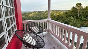 A balcony with two wicker chairs and a red wall. - Experience Puerto Rico's Charm in style with modern comforts.  (Luyando)