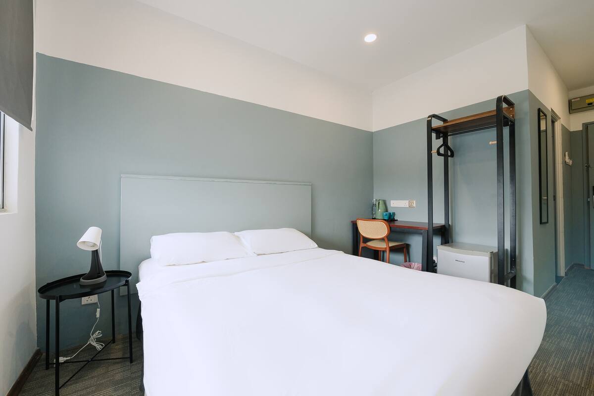 Une chambre d’hôtel avec un grand lit, un bureau avec une chaise, une petite table avec une lampe et un dressing.