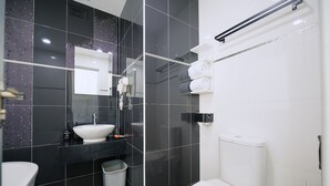 A modern bathroom with a white sink, black tiles, a glass shower enclosure, and a towel rack. - The Concept Hotel Melaka City (Malacca City)