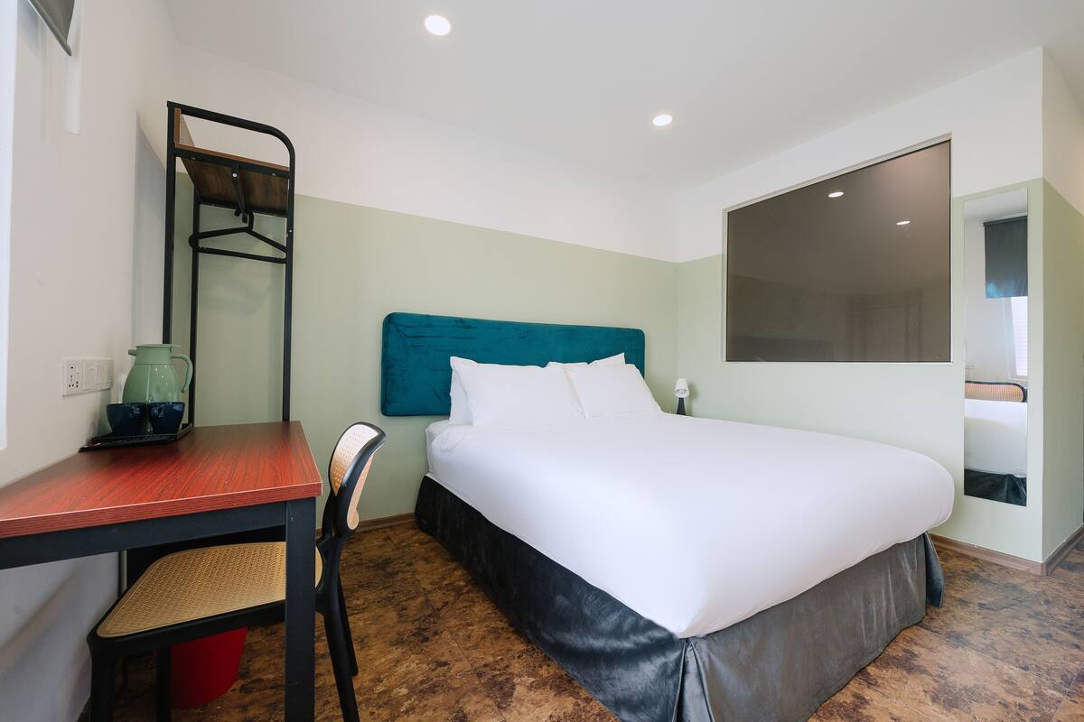 Une chambre d’hôtel équipée d’un lit, d’un bureau, d’une chaise, d’un porte-manteau et d’une grande fenêtre.