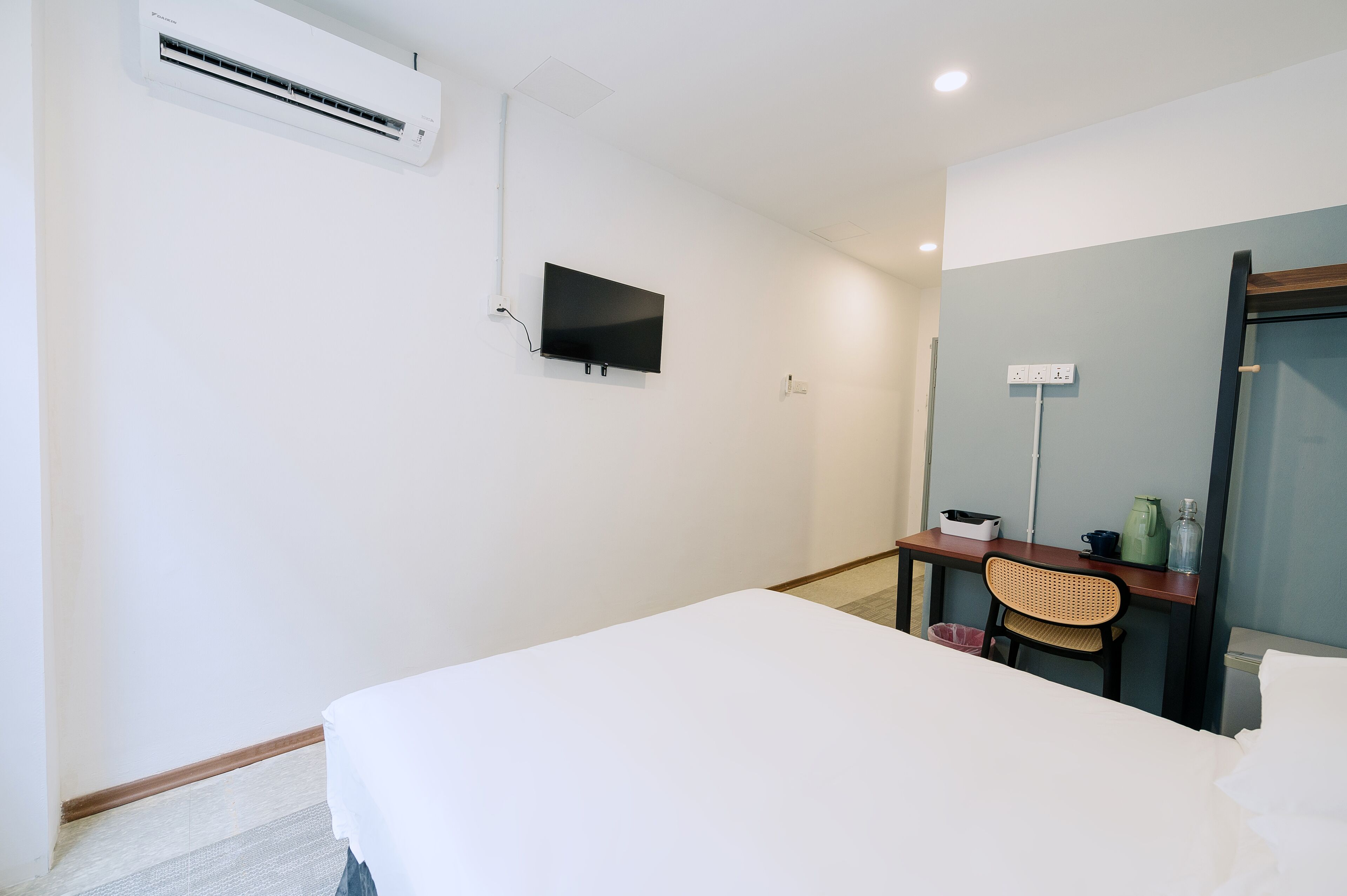 A hotel room with a bed, a desk with a chair, a television, and an air conditioning unit.