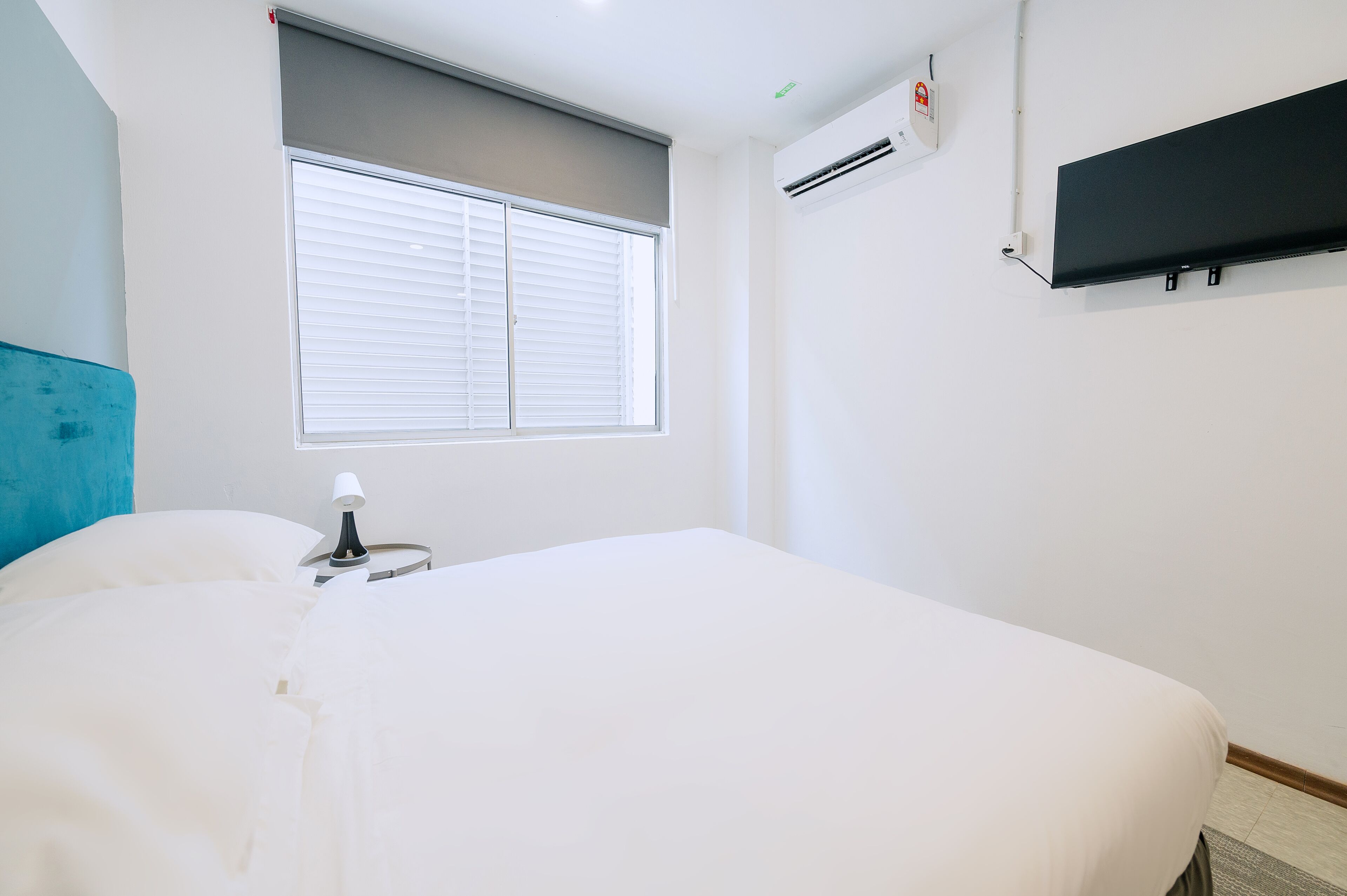 Een hotelkamer met een bed, een raam met zonwering, een airconditioner en een wandtelevisie.