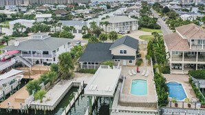 A coastal residential area with a dock, a swimming pool, and a large house with a balcony. - 5BR Waterfront Retreat with Pool, Boat Slips + Dock | Boater’s Dream House (Destin)