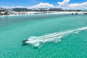 A beach with clear turquoise water, a jet ski, and a distant shoreline with buildings. - 5BR Waterfront Retreat with Pool, Boat Slips + Dock | Boater’s Dream House (Destin)