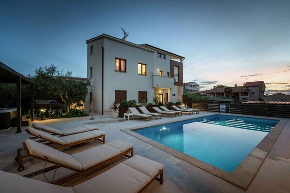 Un bâtiment moderne à deux étages doté d’une piscine, de chaises longues et d’un jardin bien entretenu.