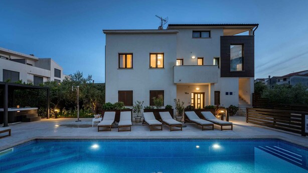 Ein modernes, zweistöckiges Haus mit Swimmingpool, Liegestühlen und einer gut beleuchteten Eingangsparte.