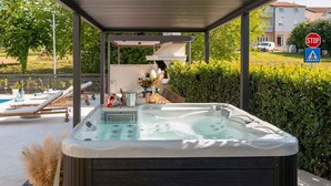 Ein Whirlpool unter einem überdachten Bereich mit Liegestühlen und einem Pool im Hintergrund.