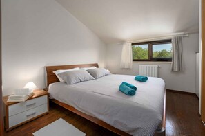 Cozy retreat with a large bed, nightstand, and window offering a view of lush greenery.