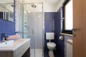 Une salle de bain moderne avec une douche à parois de verre, des toilettes blanches et un lavabo agrémenté d'une serviette rose.