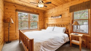 A wooden cabin bedroom with a bed, a nightstand, a lamp, and a ceiling fan.