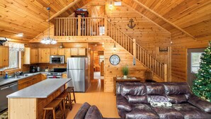 A log cabin interior with a kitchen, dining area, and living room.