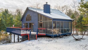 A blue cabin with a large glass window, a deck, and a chimney.