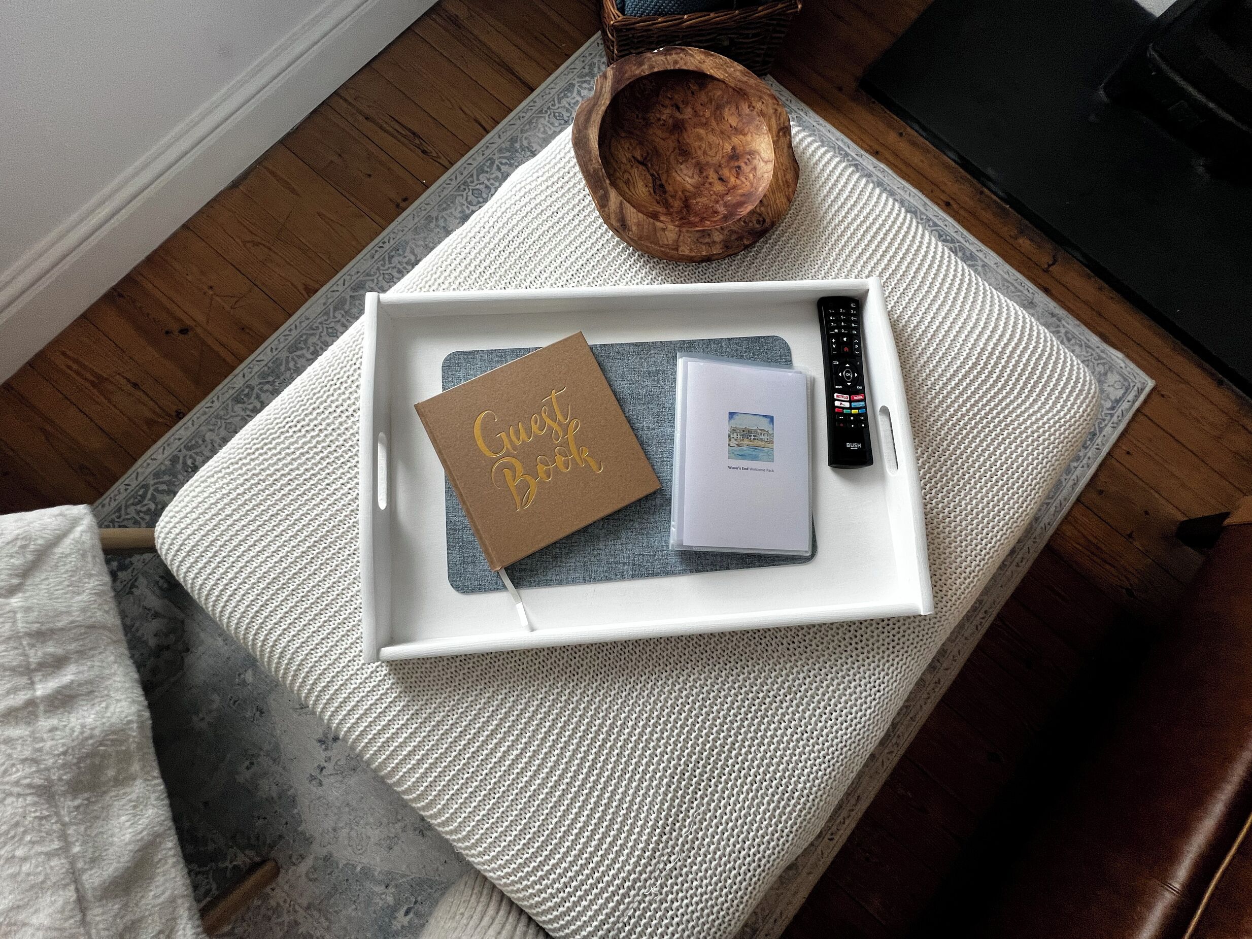 Una bandeja blanca con un libro de visitas marrón y un folleto pequeño sobre un tapete blanco con textura.