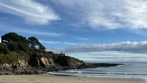 Una playa costera con acantilados rocosos, un faro y el océano.