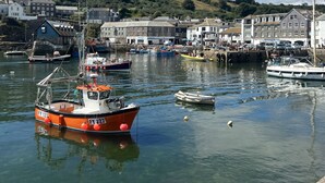 Un puerto con varios barcos amarrados, rodeado de edificios y un paisaje montañoso al fondo.