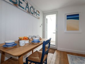 A dining area with a wooden table, striped bowls, a teapot, and oranges. A beach-themed sign is on the wall, and a framed picture is on the wall.